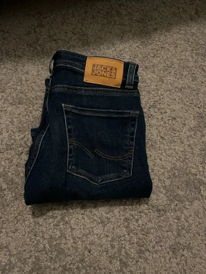 Mörkblå jeans från Jack & Jones slim fit - Snygga mörkblå jeans från Jack & Jones med klassisk femficksdesign och kontrastsömmar. Jeansen har en rak passform och är tillverkade i mjukt denimtyg som sitter skönt hela dagen.
