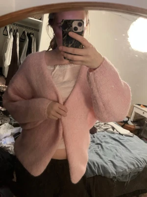 Ljusrosa fluffig kofta - Supermjuk och oversized ljusrosa kofta med v-ringning och långa ärmar. Koftan har en enkel och stilren design, perfekt att slänga på sig över en topp. Materialet ser ut att vara fluffigt och mysigt.