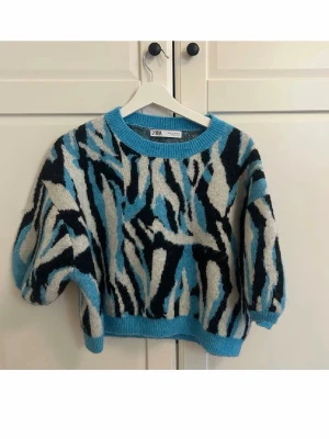 Blå och svart mönstrad stickad tröja Zara - Storlek L men skulle säga att den sitter som en      S/M. Stickad tröja från Zara med coolt abstrakt mönster i blått, svart och vitt. Tröjan har kortare, boxig passform och vida ärmar med ribbade muddar och rund hals. Perfekt för dig som gillar statement-plagg och vill sticka ut. 