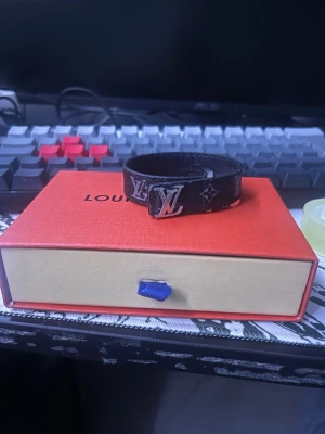 Svart läder armband - Svart armband med silvrigt fäste, använd skick men tillhörande dustbag och box med papper. 