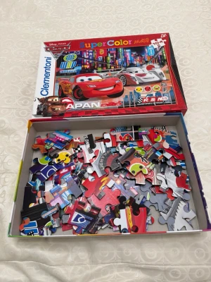 Disney Pixar Cars pussel 104 bitar - Säljer ett färgglatt Disney Pixar Cars pussel från Clementoni med 104 bitar. Motivet visar Blixten McQueen och andra bilar i en neonupplyst stadsmiljö. Pusselbitarna är av kartong och kommer i originalkartong med tydlig bild på locket.