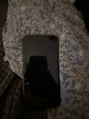 Svart iPhone 11 från Apple - Säljer en svart iPhone 11 med stilren design och rundade kanter. Baksidan är i glas med två kameror i hörnet och den klassiska Apple-loggan. Perfekt för dig som vill ha en snygg och kraftfull mobil med modern känsla. Den har 83 % batterihälsa