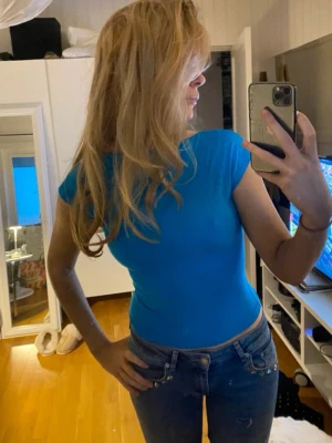 Blå croppad topp med öppen rygg - Snygg blå croppad topp med tight passform och öppen rygg. Toppen har korta ärmar och är perfekt för dig som vill sticka ut med en enkel men cool stil. Passar till både jeans och kjol för en trendig look.