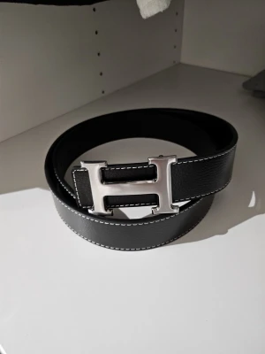 Svart H bälte  - Snyggt svart H bälte som passar för många outfits. Perfekt accessoar för dig som gillar klassisk design och lyxiga detaljer. Dm vid intresse!