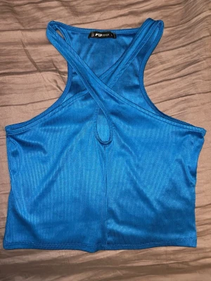 Blå croppad topp från FB Sister - Snygg blå croppad topp från FB Sister med ribbad struktur och korsade axelband framtill. Toppen har en liten cut-out detalj vid bröstet och är tillverkad i ett stretchigt syntetmaterial som sitter bekvämt. Perfekt för dig som gillar trendiga och sportiga plagg.