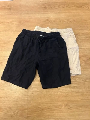 Två-pack Linen Shorts - NYPRIS: 300kr/st     Två par enkla shorts i marinblå och beige med elastisk midja och snörning. Perfekta för sommaren, tillverkade i mjukt bomullstyg för maximal komfort. Klassisk passform med sidofickor, passar till allt från chill till häng med vänner. Storlek 170.
