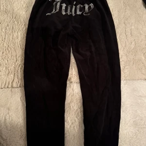 Svarta Juicy Couture mjukisbyxor - Svarta mjukisbyxor från Juicy Couture i mjuk velour med strassdetaljer och Juicy-logga bak. Byxorna har snörning i midjan och raka ben med mudd längst ner 