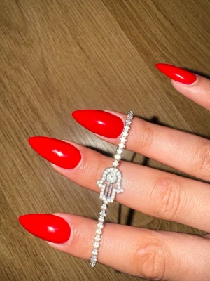 Swarovski Silverarmband med Hamsa och stenar - Snyggt silverfärgat armband med gnistrande stenar och en Hamsa-hand dekorerad med små kristaller. Justerbar kedja med detalj och ett elegant, modernt uttryck. Perfekt accessoar för dig som gillar trendiga smycken med symbolik.