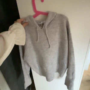 Grå hoodie med huva och snörning - Mysig grå hoodie med huva och snörning framtill. Tröjan har långa ärmar och ribbade muddar vid ärmslut och nederkant. Perfekt för kyliga dagar och enkel att matcha med jeans eller mjukisbyxor.