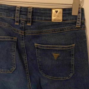 Blå jeans från Guess - Snygga blå jeans från Guess med klassisk och  logga bak. Jeansen har breda ben och normal midja, tillverkade i jeansmaterial med kontrastsömmar. Perfekt för dig som gillar en avslappnad och trendig look. W25