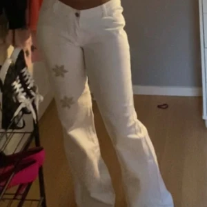 Vita bootcut jeans med blommor - Säljer ett par vita jeans med bootcut-modell och snygga blommor broderade på ena benet. Byxorna är lågmidjade!💞Skriv för fler bilder🥰