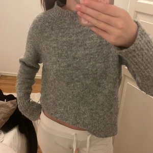 Grå stickad tröja med rund hals - Mysig grå stickad tröja med rund hals och långa ärmar. Tröjan har en enkel och klassisk design med ribbade muddar vid ärmslut och nederkant. 