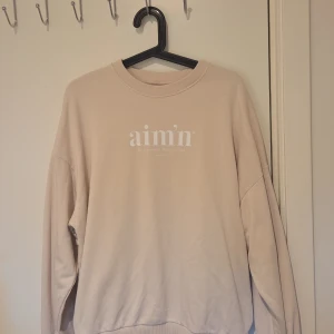 Beige sweatshirt från Aim'n - Säljer en beige sweatshirt från Aim'n med tryckt logga framtill. Tröjan har rund hals, långa ärmar och ribbade muddar vid hals, ärmslut och nederkant. Använd ett fåtal gånger. Cremefärgad