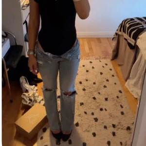 Ljusblå slitna bootcut jeans - Säljer ett par ljusblå jeans med bootcut passform och snygga slitningar vid knäna. Jeansen har låg midja och klassisk femficksdesign. Perfekta för dig som gillar en avslappnad och trendig stil.