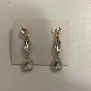 Glittriga örhängen med kristaller - Snygga örhängen med tre stora, gnistrande kristaller i olika former på rad. Infattningarna är i guldton och designen är elegant och iögonfallande. Perfekta för dig som vill sticka ut med lite extra bling.