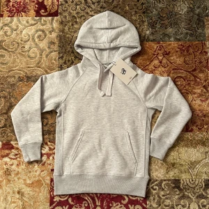 Ljusgrå hoodie från Russemerch  - Snygg ljusgrå hoodie från Russedress i storlek small. Tröjan har huva med snörning, magficka och ribbade muddar. Perfekt för chill dagar och har en stilren logga på ärmen. Mjuk och skön bomullsmix som passar dig som gillar enkel och clean stil. Helt ny. 