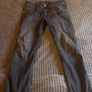 Replay Anbass svarta slim jeans - Svarta Replay Anbass jeans med slim fit och klassisk femficksdesign. Jeansen har snygga detaljer på bakfickorna och är tillverkade i ett mjukt jeansmaterial. Passformen är smal och midjan är normal. Perfekta för dig som gillar stilrena och moderna jeans.