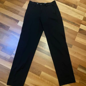 Svarta kostymbyxor  - Snygga svarta kostymbyxor med klassisk rak siluett och diskreta fickor både fram och bak. Byxorna har bälteshällor och knappstängning i midjan. Perfekta för en clean och stilren look, passar dig som gillar enkelhet och tidlös stil. Relaxed passform, lutar åt det större hållet för mig. Knappt använda. Skriv ifall du vill ha fler bilder. Kan gå ner i pris vid snabb affär.  (W29, L34) 