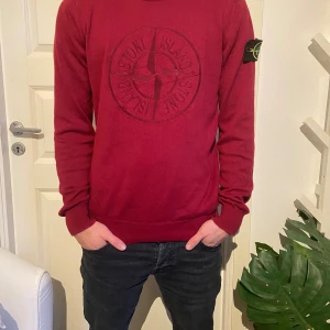 Vinröd Stone Island stickad tröja - Säljer en vinröd stickad tröja från Stone Island med stort broderat logomärke på bröstet och klassisk patch på ärmen. Tröjan har rund hals, ribbade muddar och lång ärm. Perfekt för dig som gillar streetwear och snygga detaljer. Lappen i är borta tyvär 