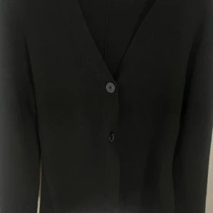 Svart v ringad kofta med knappar - Supersnygg och skön svart v ringad kofta med knappar både framtill o vid ärmar. Den är använd några gånger och är därför lite nopprig (syns på bilderna), annars jättebra skick. De är ett tjockt och skönt material och formar midjan supersnyggt! 🥰