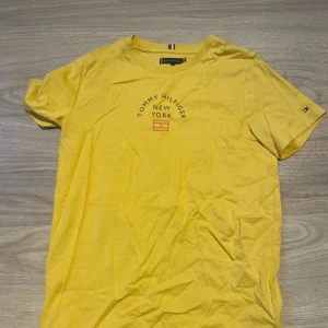 Gul t-shirt Tommy Hilfiger - Snygg gul t-shirt från Tommy Hilfiger med tryck 'Tommy Hilfiger New York' på bröstet och diskret logga på ärmen. Klassisk rund hals och korta ärmar. Mjuk bomullskvalitet som känns skön mot huden. Perfekt för dig som gillar färg och stil.