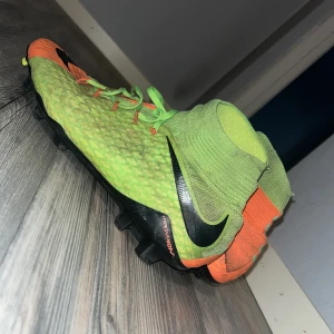 Nike Hypervenom fotbollsskor orange/grön - Nike Hypervenom fotbollsskor med cool design i orange och grön, svarta detaljer och högt strumpliknande skaft. Skorna har snörning och mönstrad ovandel i syntetmaterial för bra grepp på planen. Perfekt för dig som vill sticka ut på matchen. Pris kan diskuteras..
