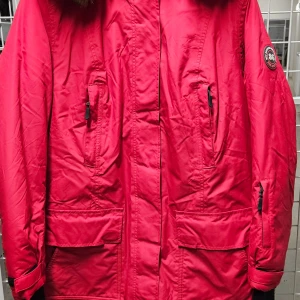 Röd parkas från Bonprix Collection - Röd parkas från Bonprix Collection med svart patch på ärmen, flera fickor med dragkedja och lock, samt svarta ribbade muddar vid ärmsluten. Jackan har huva och är perfekt för kalla dagar. Snygg och funktionell design med streetkänsla.