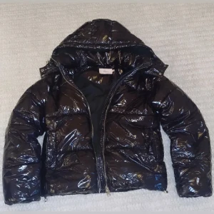 Glansig svart pufferjacka från Nelly - Säljer min snygga vinterjacka från Nelly med huva och dragkedja. Perfekt nu inför vintern. Säljer den eftersom att jag köpt en ny vinterjacka. 