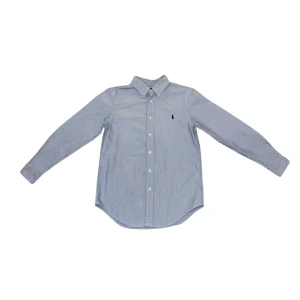 Blå skjorta från Ralph Lauren - Klassisk ljusblå skjorta från Ralph Lauren med button-down krage och broderad logga på bröstet. Skjortan har lång ärm, vita knappar och är tillverkad i mjuk bomull. Perfekt för dig som gillar stilrena och tidlösa plagg. Förhandla gärna 