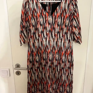 Mönstrad långklänning från Turnover - Säljer en långklänning från Turnover med coolt abstrakt mönster i svart, rött, beige och vitt. Klänningen har v-ringning och trekvartsärmar. Materialet känns lätt och flowy, perfekt för dig som gillar färg och mönster.