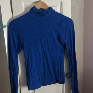 Kornblå ribbad polotröja, xs - Säljer en kornblå polotröja med ribbad struktur och lång ärm. Tröjan har en tight passform och är tillverkad i ett stretchigt material som sitter snyggt på kroppen. 