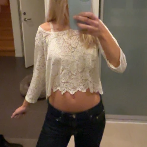 Vit spetsblus från Monki - Säljer en vit croppad blus från Monki i storlek Small. Blusen är i spets med blommigt mönster och har trekvartsärm. Perfekt för dig som gillar romantisk och feminin stil. Superfin att styla med höga jeans!