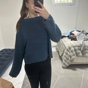 Mörkblå stickad tröja från 157 - Mysig mörkblå stickad tröja från 157 med avslappnad passform och lite croppad längd. Tröjan har rund halsringning och långa ärmar, perfekt för lager-på-lager under kyliga dagar. Tröjan har ett litet hål på framsidan 