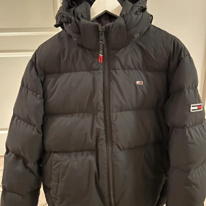 Svart pufferjacka Tommy Jeans S - Svart, otroligt varm och skön, vinterjacka från Tommy Jeans. Tvättad 1 ggr. Har försökt syna jacka nog och det enda jag hittar är ett litet märke/skav, se bild 3. Märket/skavet är så litet så jag missade det vid första genomgången av jackan men därav något lägre p