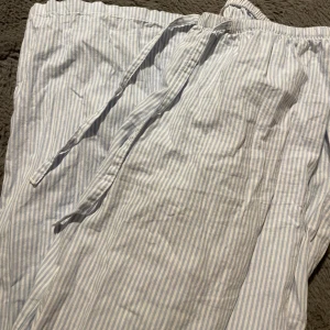 Randiga linnebyxor från H&M  - Luftiga linnebyxor från H&M i storlek XS. Byxorna har ljusblå och vita ränder, elastisk midja med snörning och är perfekta för varma dagar. Tillverkade i mjukt linne för en chill och bekväm vibe.