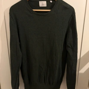 Mörkgrön stickad tröja från Bläck - En stilren mörkgrön stickad tröja från Bläck i storlek M. Tröjan har rund halsringning, ribbade muddar och lång ärm. Perfekt för lager-på-lager och enkel att matcha med jeans.