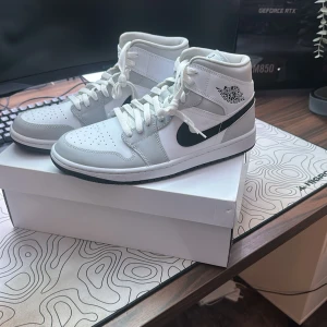 Air Jordan 1 Mid Grey Fog sneakers - Nike Air Jordan 1 Mid i färgen Grey Fog/White med svarta detaljer. Klassisk high-top siluett med vit och ljusgrå ovandel i skinn, svart swoosh och Air Jordan-logga på sidan. Perforerad tåbox och vita skosnören. Riktigt clean och stilren sneaker för dig som gillar streetwear. Har testat dom 1 gång och insåg att det var försmå. Sen har dom bara stått i min garderob i 2 år. Original pris var: 3499