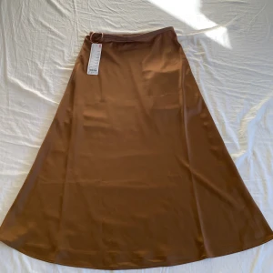 Brun satin kjol från Uniqlo - Säljer en snygg brun satin kjol från Uniqlo. Perfekt att styla med sneakers eller boots för en chill look.