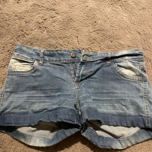 Blå jeansshorts från Chillin, stl S - Säljer ett par klassiska blå jeansshorts från Chillin i storlek S. De har fem fickor, uppvikta benslut och snygga slitningar för en avslappnad look. Perfekta för varma dagar och enkla att matcha med allt. Dragkedja och knapp framtill.