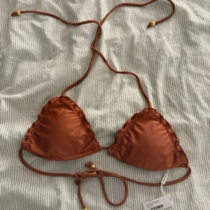 Brun bikiniöverdel från NLY Beach - Snygg brun trekantsbikini från NLY Beach med tunna snören som knyts i nacken och ryggen. Bikinin har små guldfärgade detaljer på snörena och är tillverkad i mjukt syntetmaterial. Perfekt för strandhäng och soliga dagar.