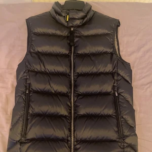 Svart dunväst Parajumpers Sheen M - Snygg svart dunväst från Parajumpers modell Sheen. Västen har quiltad design, hög krage och dragkedja framtill. Två dragkedjefickor på sidorna och coolt Parajumpers-märke i nacken. Perfekt för lager-på-lager och streetstyle. Kvitto finns! Bara att skriva vid frågor och priset går såklart att diskutera!