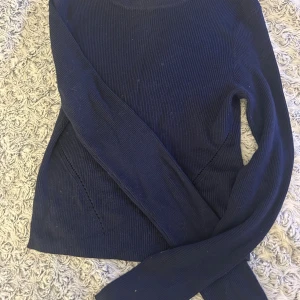 Mörkblå stickad tröja med knyt - Snygg mörkblå stickad tröja med långa ärmar och coola knyt-detaljer på sidorna. Tröjan har en rund halsringning och ribbade muddar vid ärmslut och nederkant. Perfekt för dig som gillar en enkel men ändå unik look.