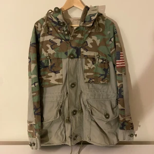Ralph Lauren Denim & Supply Militärjacka Fieldjacka - Ralph Lauren Denim & Supply Militärjacka Fieldjacka  Unik camouflage- och khakifärgad fältjacka från Ralph Laurens Denim & Supply-kollektion. Vintageinspirerad design med amerikansk flaggpatch på ärmen, stora fickor och justerbar midje- och fållsnörning.  Priset kan diskuteras vid ett snabbt köp  Fraktar inom 24 timmar  Perfekt för dig som gillar vintage, archive-stil. Storlek: S Skick: Mycket bra – inga defekter, bara naturligt slitage som hör till stilen.