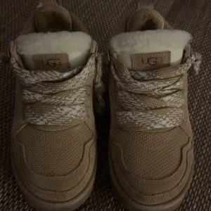 UGGS SKOR - Snygga beige sneakers från UGG (som gick vitalt på TikTok förra året) med fluffigt fuskpälsfoder och grova snören i beige och vitt mönster. Skorna har platt sula, rund tå och detaljer i mocka och textil. Skorna är i jättebra form, används några gånger i storlek 38🌸