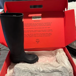 Hunter navy höga stövlar strl 36 - Snygga höga stövlar från Hunter i marinblått. Modellen är Womens Org Tall med klassisk rund tå, platt sula och justerbart spänne upptill. Tillverkade i slitstark syntet som håller dig torr och stilren under regniga dagar.