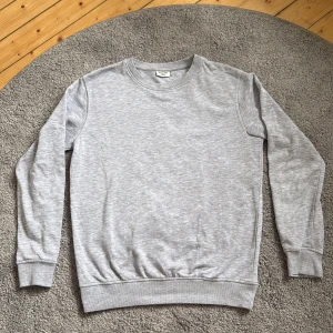 Grå sweatshirt från Kappahl i storlek 158/164 (XXS) - En basic grå sweatshirt från Kappahl i mjuk bomullsmix. Tröjan har rund halsringning, ribbade muddar vid ärmslut och nederkant samt lång ärm. Inga tecken på användning, anledning till att denna tröja säljs är på grund av utväxt. 