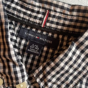 Rutig skjorta Tommy Hilfiger svart/vit - Snygg svartvit rutig skjorta från Tommy Hilfiger i 100% bomull. Klassisk button-down krage, vita knappar och broderad logga på bröstet. Perfekt för dig som gillar stilrena och tidlösa plagg. Hör hjärna av er vid intresse och priset är alltid förhandlingsbart.