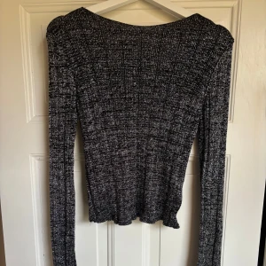 Glittrig svart långärmad topp NA-KD - Glittrig svart långärmad topp från NA-KD i storlek S. Djup rygg med en ribbad struktur. Endast använd fåtal gånger 