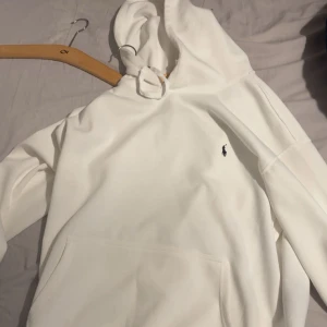 Vit hoodie från Ralph Lauren - Säljer en stilren vit hoodie från Ralph Lauren med klassisk huva och känguruficka. Tröjan har en liten broderad logga på bröstet och är perfekt för en clean och avslappnad look. Storlek XL men passar XXL 
