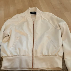 Vit bomberjacka från Bik Bok - Snygg vit bomberjacka från Bik Bok i storlek S. Jackan har en stilren design med dragkedja i guld, ribbade muddar och två fickor framtill. Materialet är slätt och känns mjukt, perfekt för dig som vill ha en clean look. Aldrig använt o köpt för 300 
